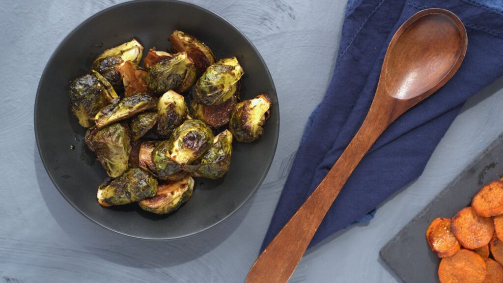 Roasted brussels sprouts in a black bowl and a wooden spoon.