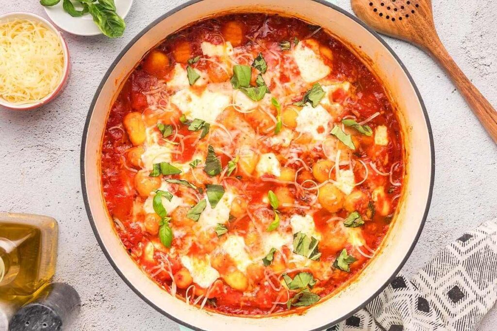 A pot of baked gnocchi alla sorrentina in tomato sauce topped with melted cheese and fresh basil.