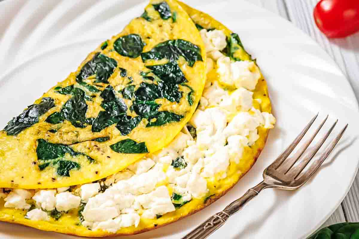 A spinach and feta cheese omelette folded on a white plate with a fork beside it.