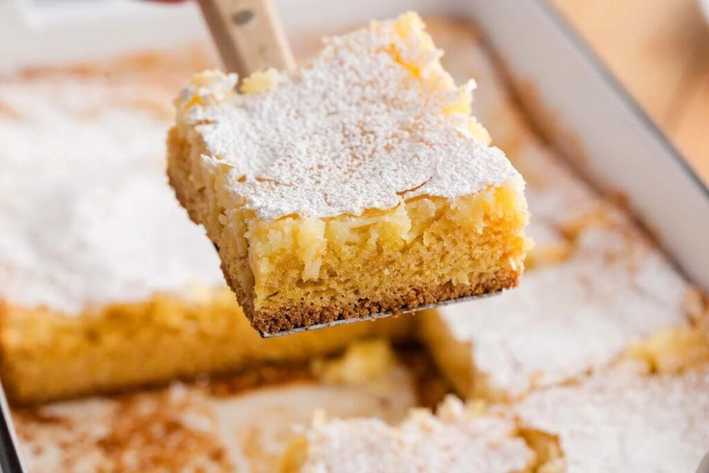 A gooey butter cake square dusted with powdered sugar, showing its rich, buttery layers.