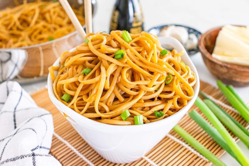 Hibachi noodles topped with green onions on a bamboo mat.