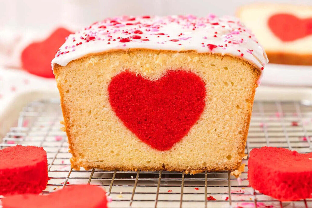 A cake loaf with a red heart baked inside, topped with white icing and pink sprinkles.