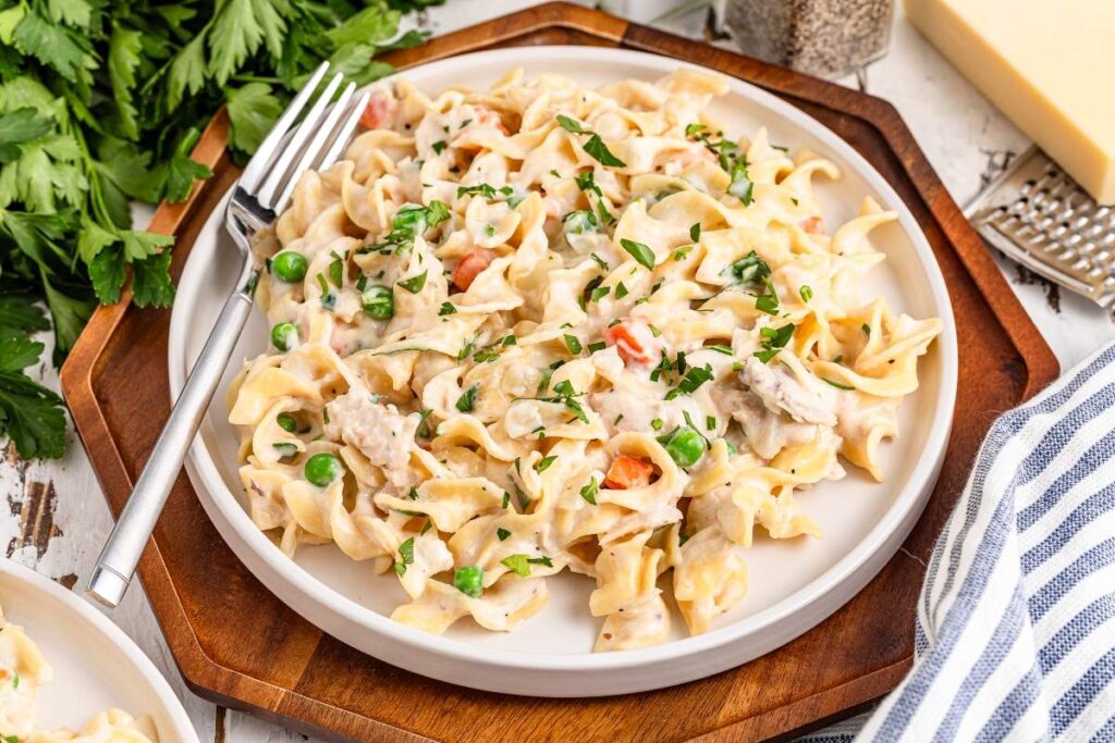 Homemade tuna helper with tuna, peas, and carrots, topped with parsley, fork on the left.