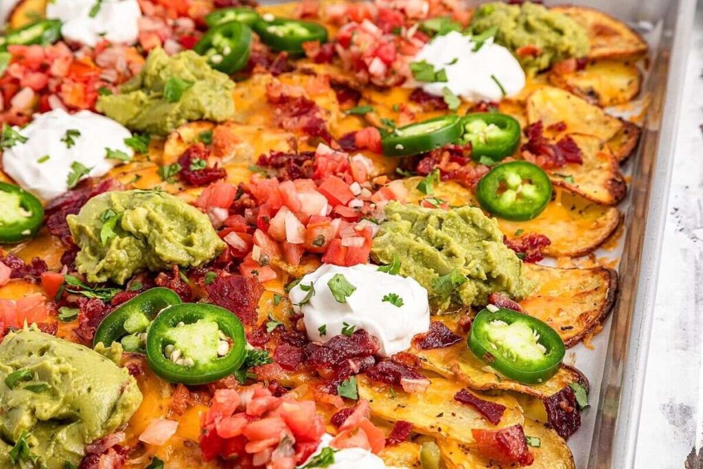 Close-up of loaded Irish nachos topped with jalapeños, guacamole, sour cream, diced tomatoes, bacon bits, and melted cheese on a tray.