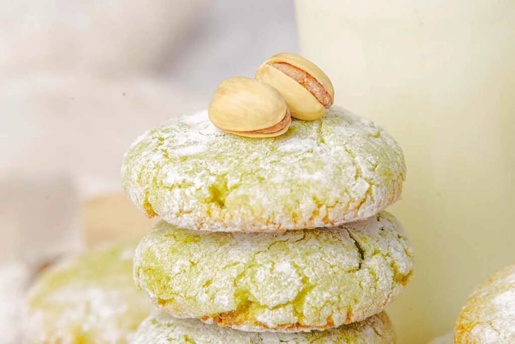 Three pistachio cookies stacked and dusted with powdered sugar, topped with whole pistachios.