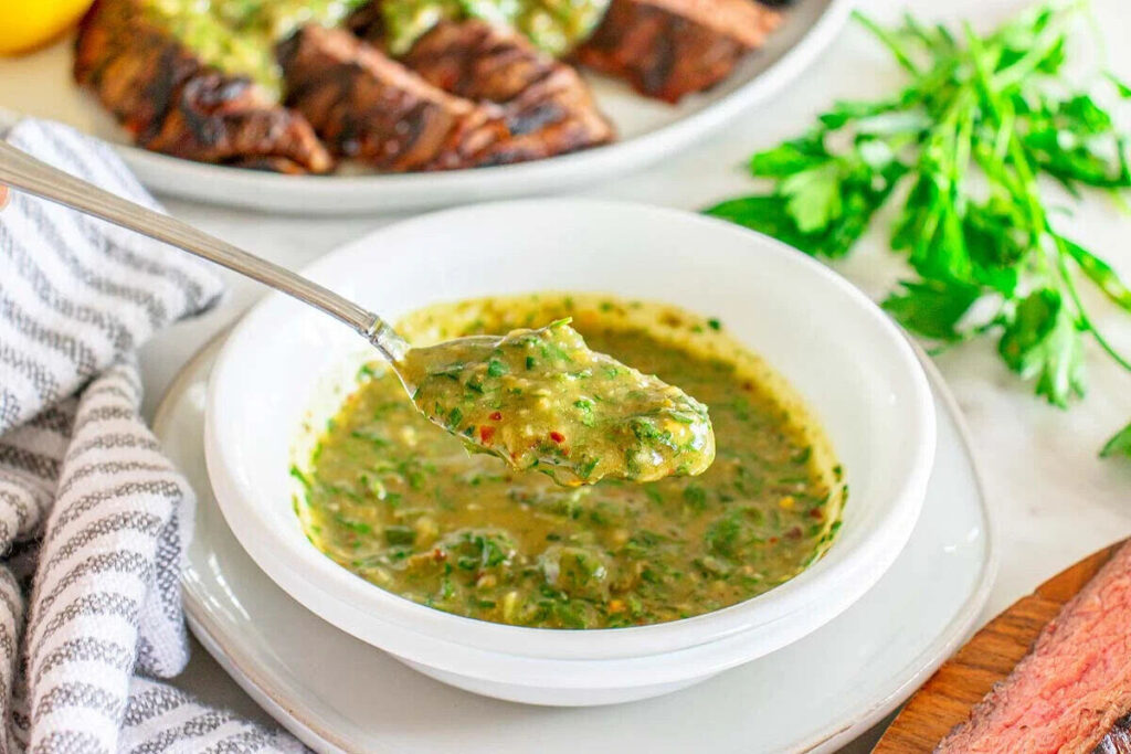 A spoonful of Italian Salsa Verde sauce is being held over a bowl.