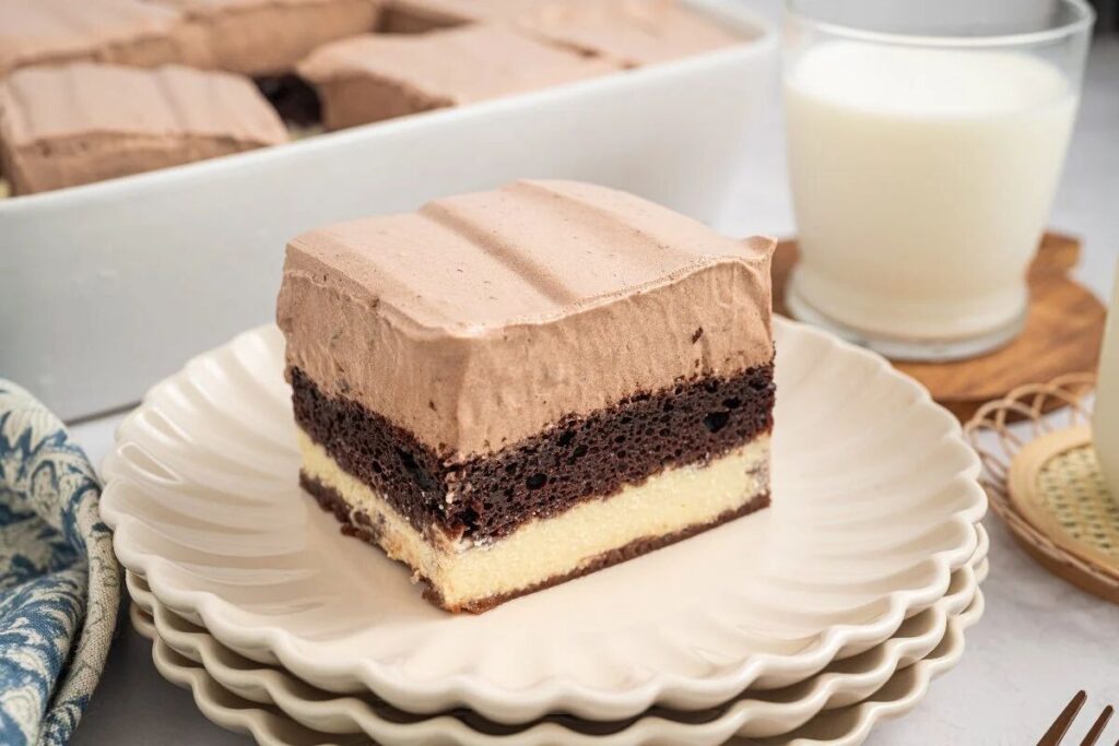 A slice of layered Italian Love Cake with chocolate and vanilla sits on plates next to a glass of milk.