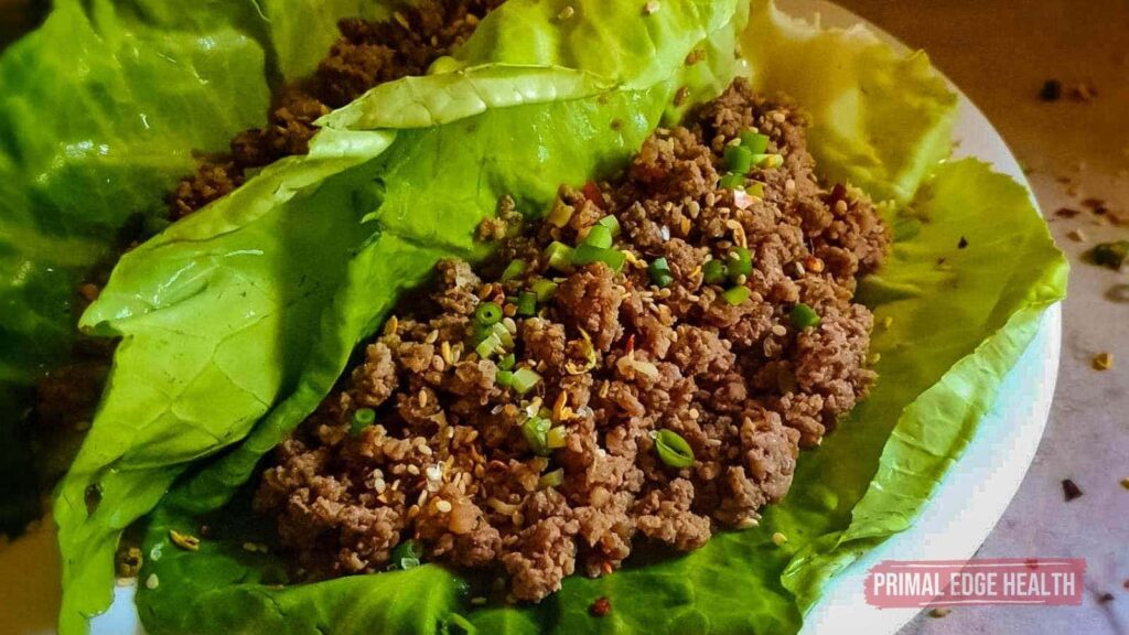 Ground beef served on lettuce leaves, garnished with chopped green onions.
