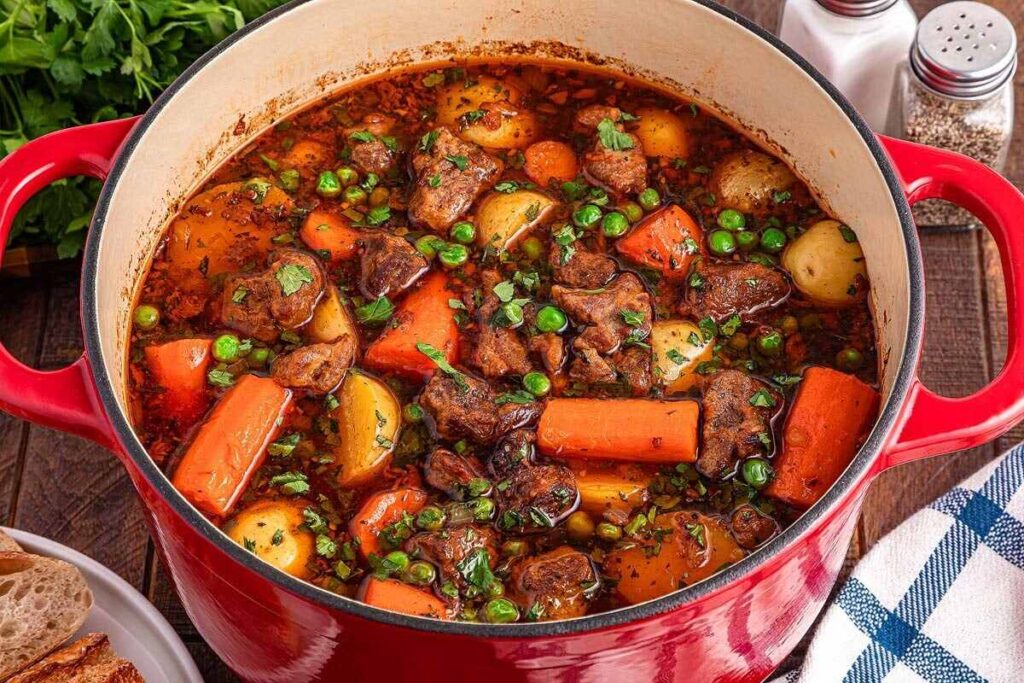 A red pot brimming with lamb stew (Irish stew) showcases tender meat chunks, carrots, potatoes, peas, and herbs in a rich broth.