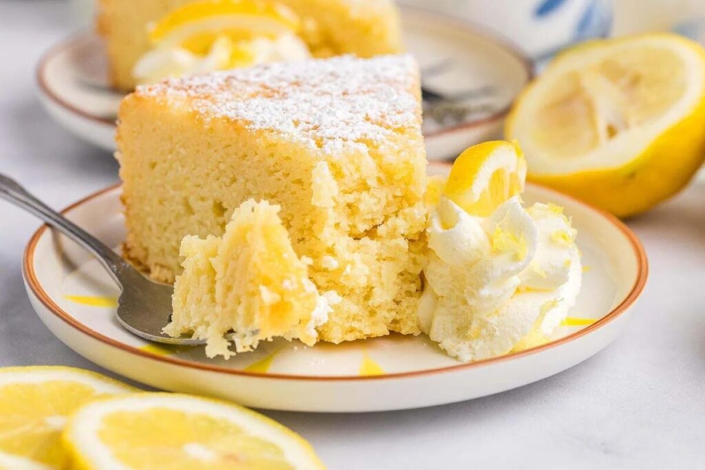 Italian Lemon Ricotta Cake with powdered sugar, whipped cream, and a lemon slice, served on a plate.