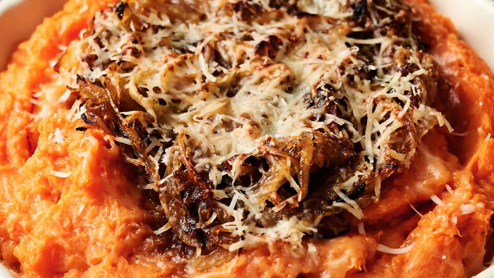 A bowl of mashed sweet potatoes topped with crispy caramelized onions and grated cheese.