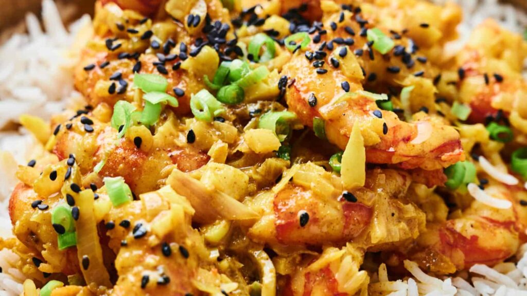 A close-up of shrimp curry served on rice, garnished with green onions and black sesame seeds.