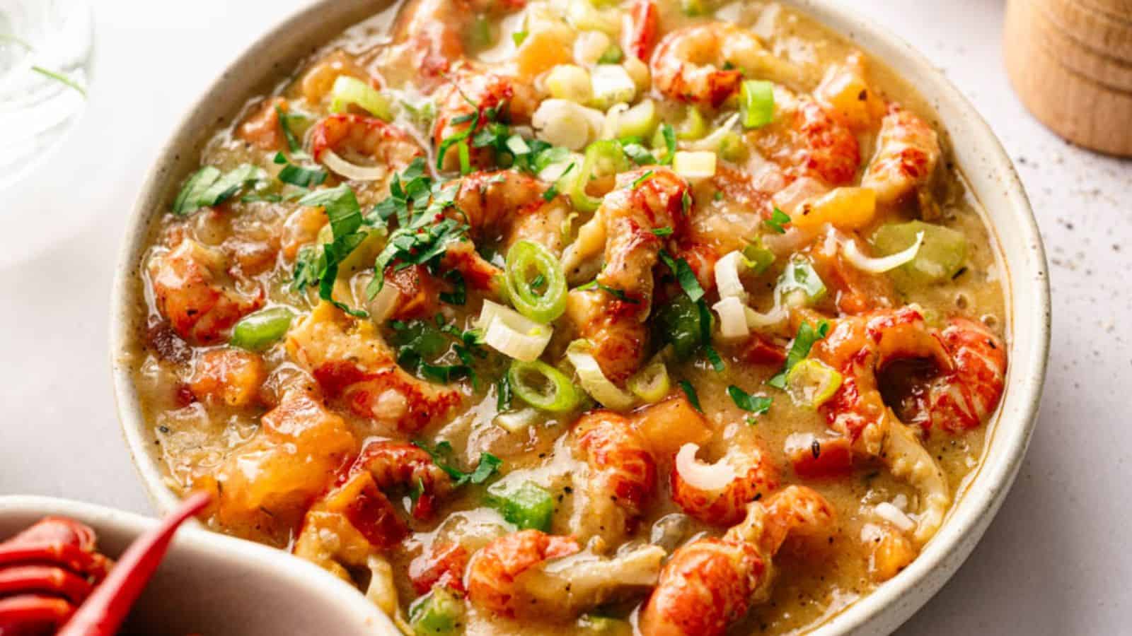 A bowl of crawfish étouffée garnished with chopped green onions and herbs, served in a light-colored dish.