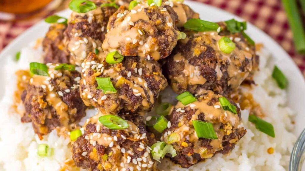 Meatballs topped with sesame seeds and sliced green onions on a bed of white rice.