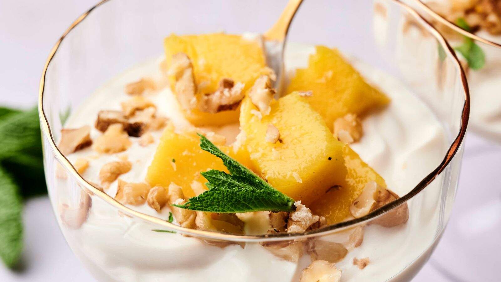 A glass dish with creamy yogurt, pineapple chunks, chopped walnuts, and a sprig of mint on top.