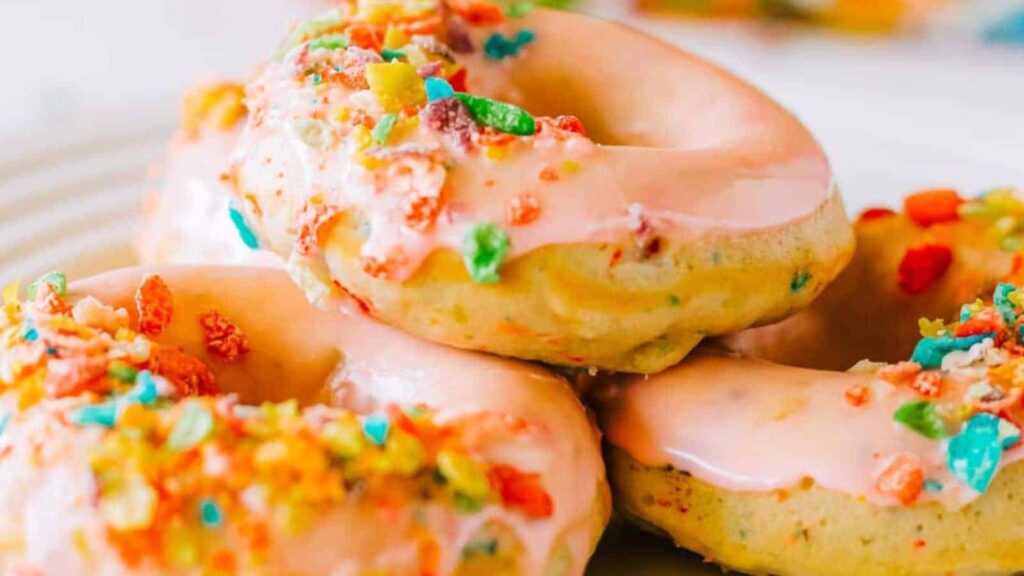 A stack of donuts with pink icing and colorful cereal toppings on a white plate.