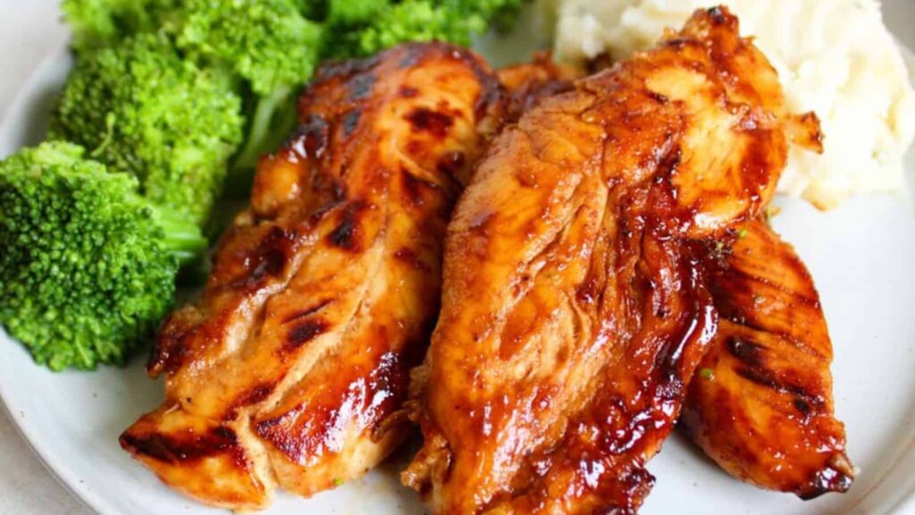 Grilled chicken breasts with a shiny glaze, accompanied by steamed broccoli florets and a serving of mashed potatoes on a white plate.