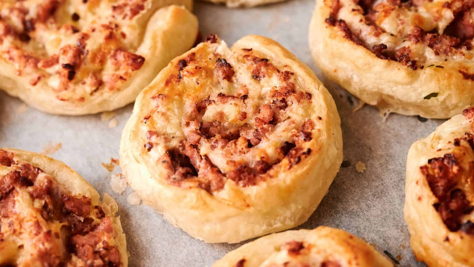 Close-up of several baked puff pastry pinwheels filled with minced meat, arranged on a baking tray lined with parchment paper.
