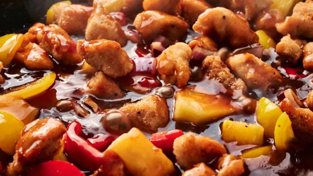 Close-up of stir-fried chicken pieces with red and yellow bell peppers in a glossy sauce.