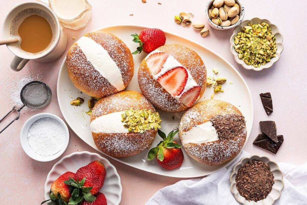 A plate of filled Italian pastries, including maritozzi cream buns with strawberries, pistachios, and chocolate.