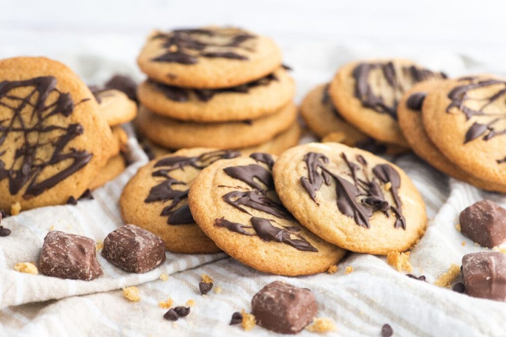 Chocolate-drizzled cookies on a striped cloth with chocolate chunks, made using fun-size chocolate bars for an indulgent treat.