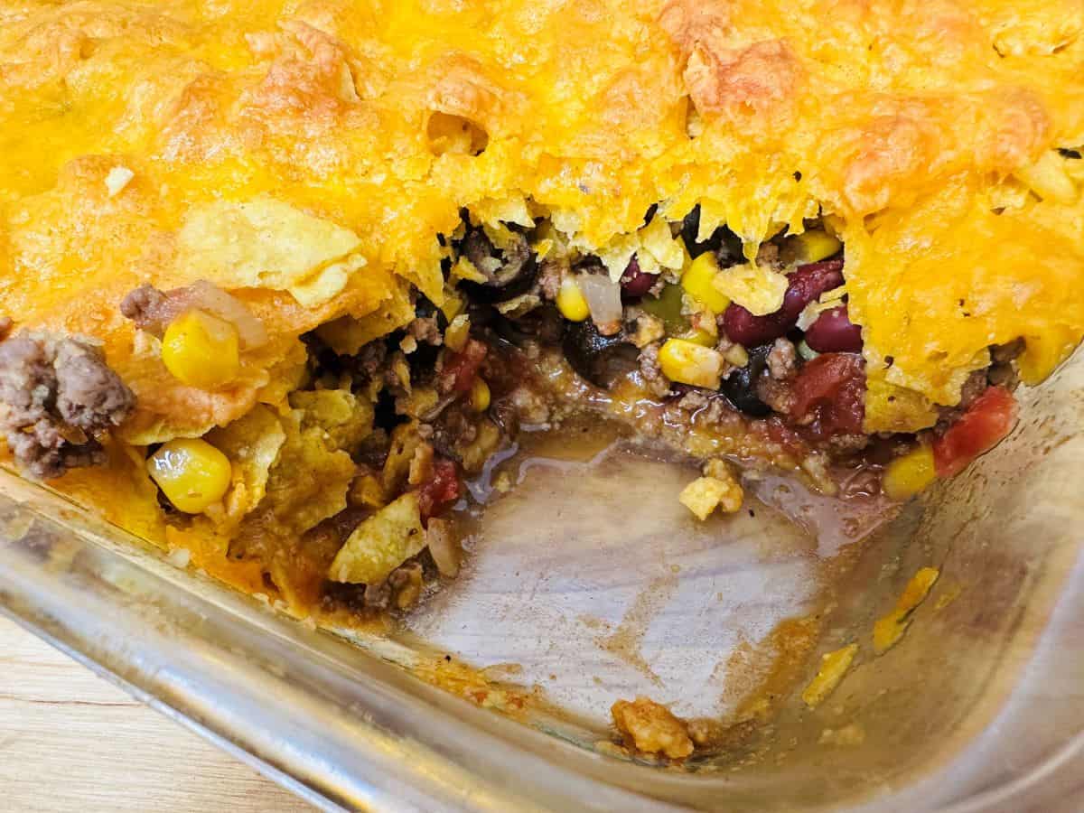 A partially served Mexican casserole in a baking dish, showing layers of corn, beans, cheese, and ground meat.