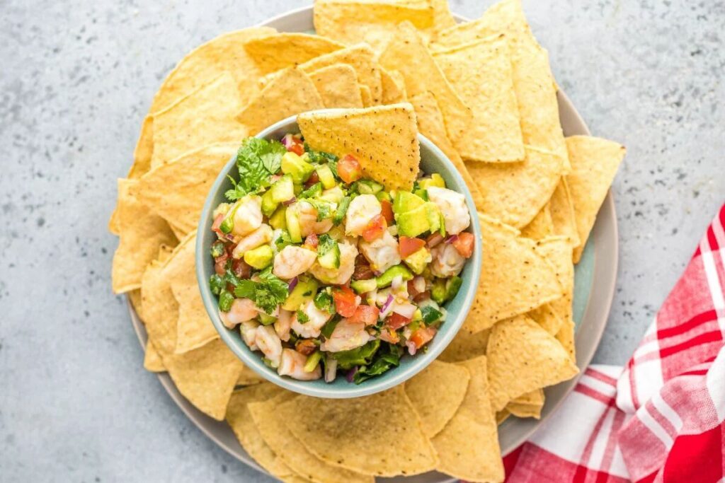 Bowl of Mexican ceviche with avocado, served with tortilla chips and a red napkin.