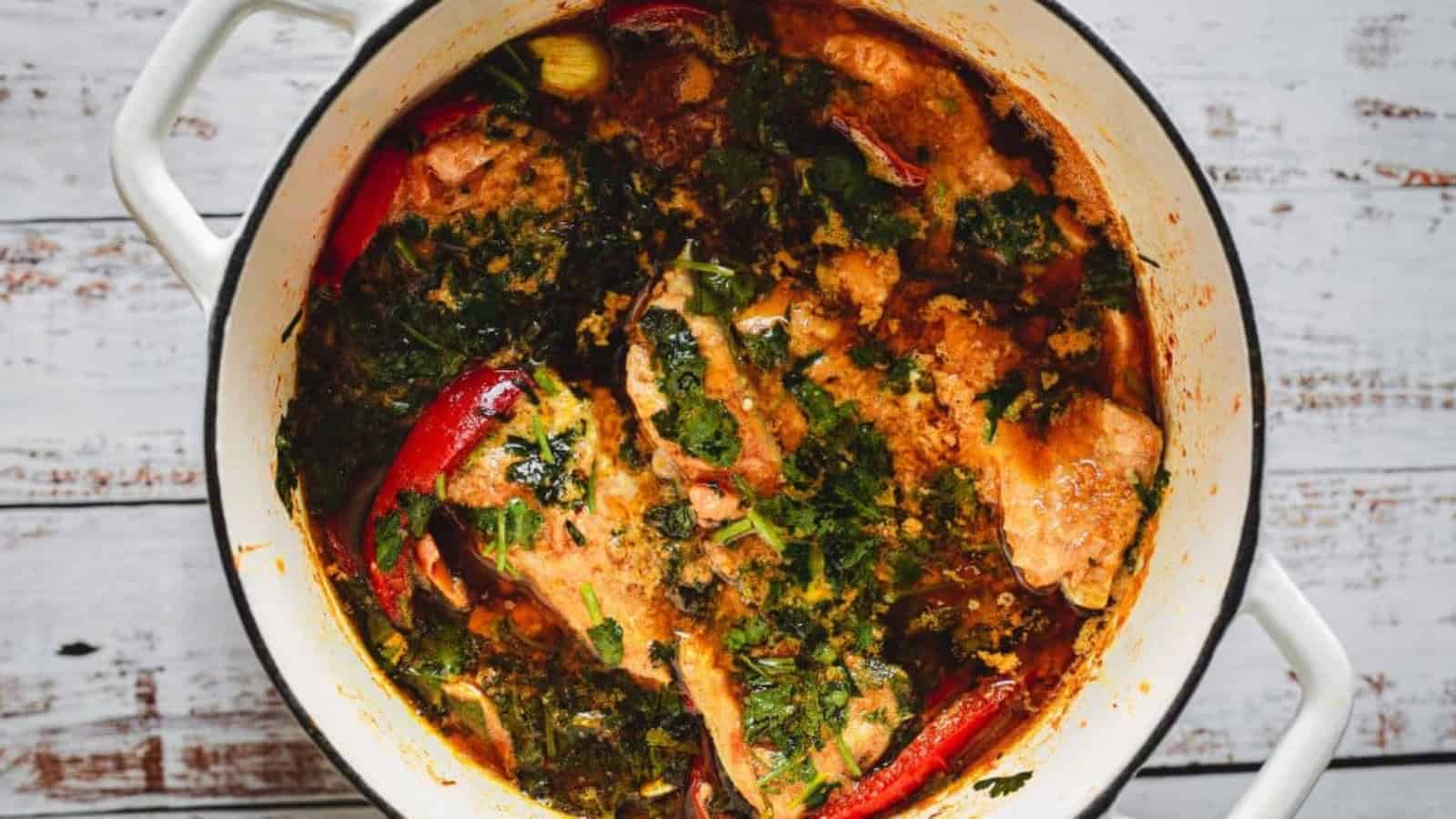 Chicken stew with herbs and whole red chilies cooking in a white pot.
