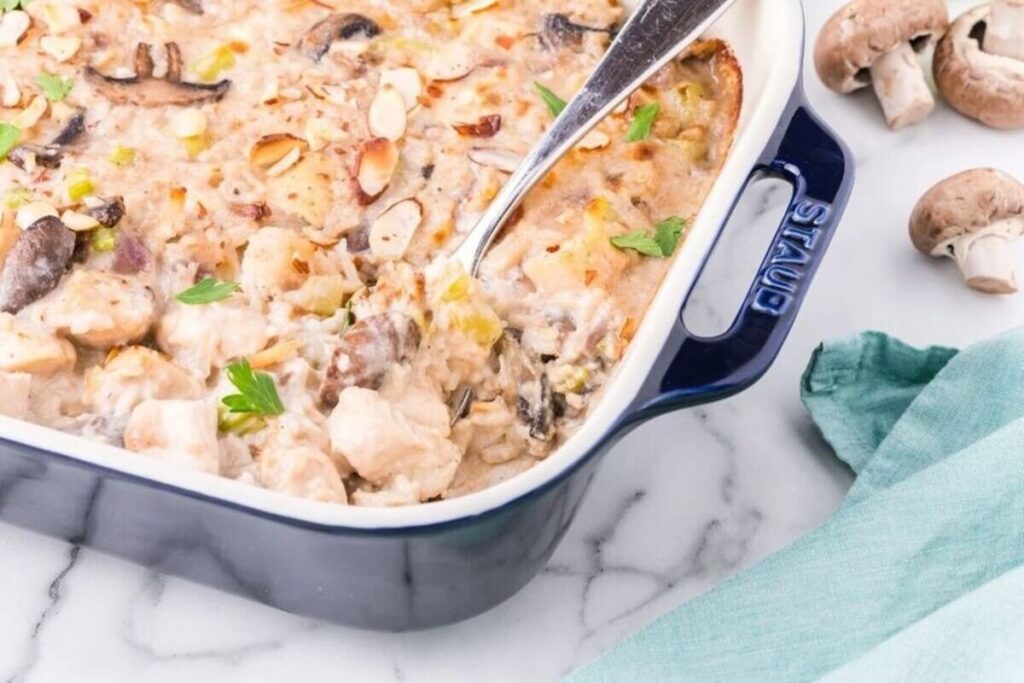 Creamy mushroom gruyere Chicken and Rice Casserole in a blue baking dish, topped with almonds, with a spoon inside.