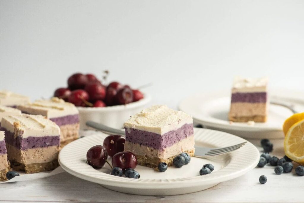 A slice of no-bake vegan cashew cheesecake with blueberries and cherries.