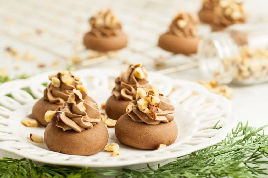 Chocolate cookies with frosting swirls and chopped nuts on a white plate.