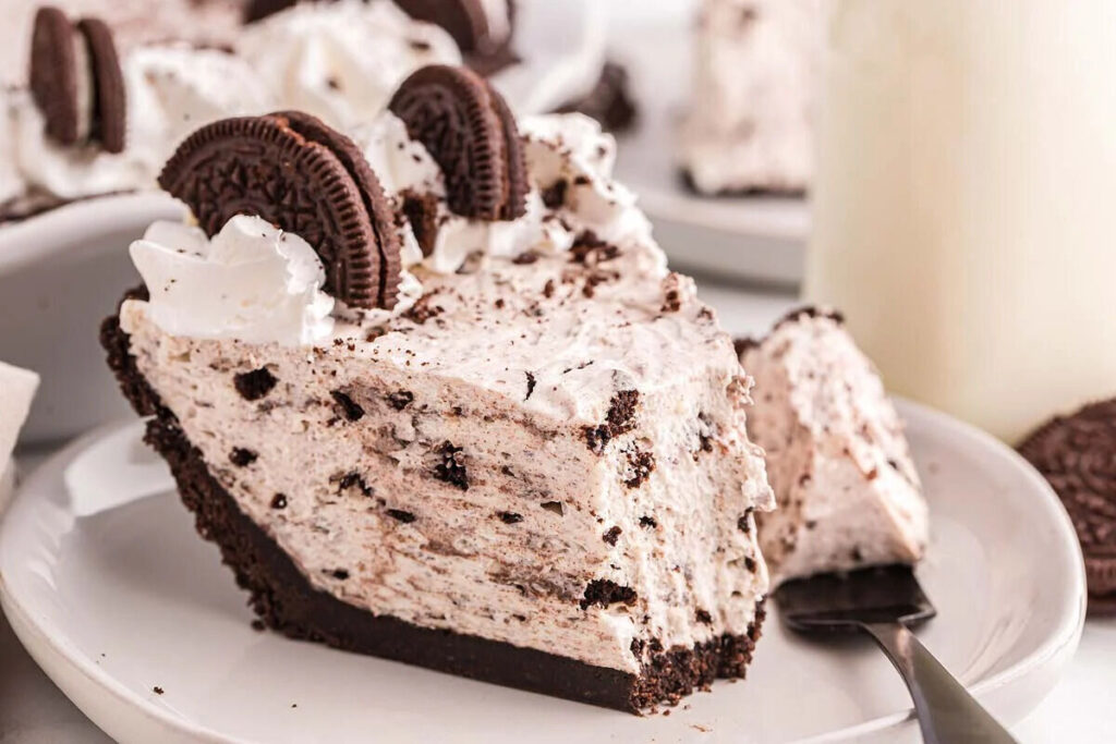 Oreo pie slice topped with whipped cream and Oreo halves on a white plate.