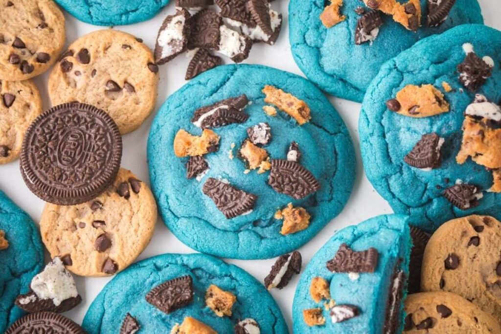 Blue Cookie Monster cookies stuffed with Oreos and chocolate chips, surrounded by whole cookies and crumbs.