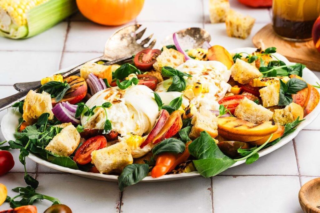 A colorful peach panzanella salad with juicy tomatoes, creamy burrata, and crunchy croutons.