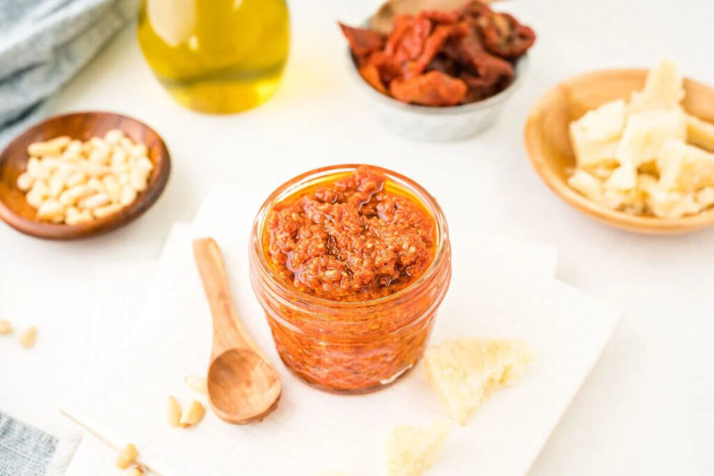 A jar of sun dried tomato pesto with a wooden spoon.