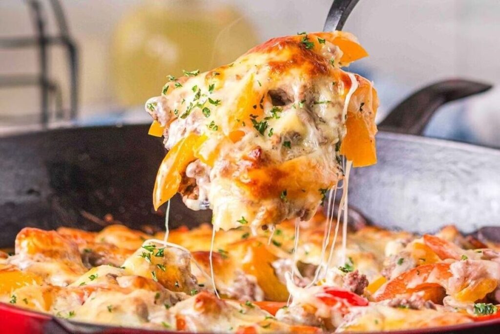 Philly cheesesteak casserole with melted cheese, bell peppers, and ground meat being served from a skillet.