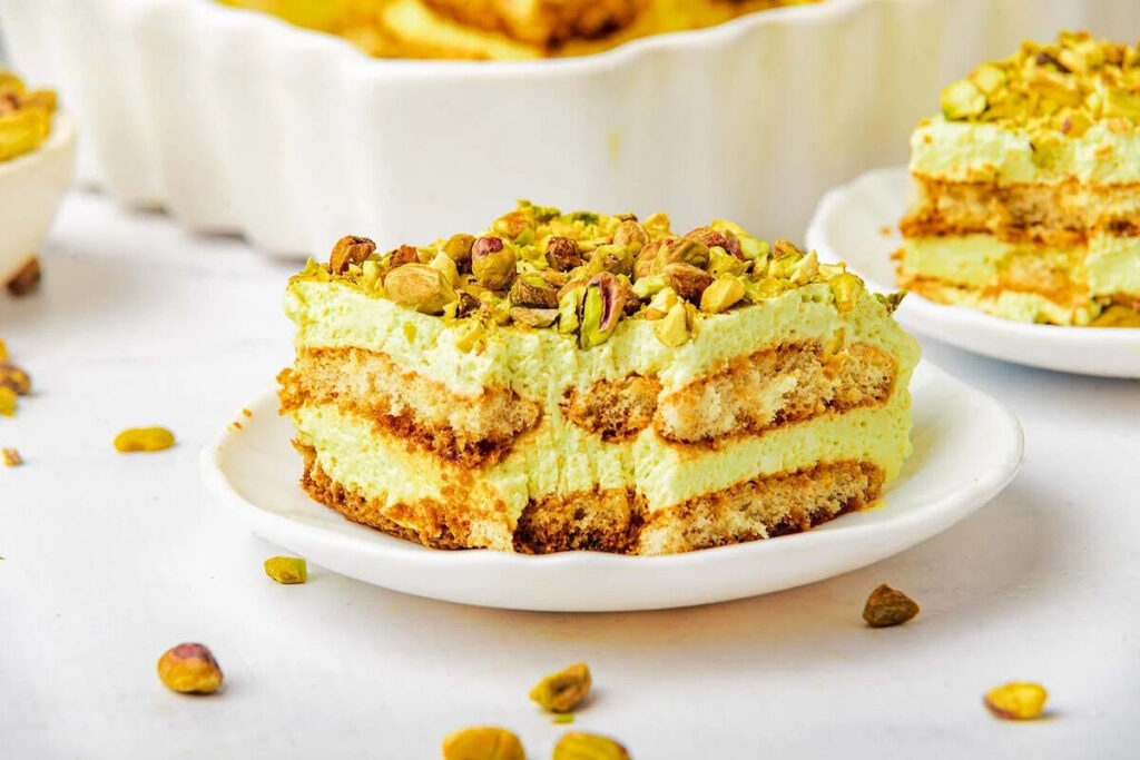 A delectable slice of pistachio tiramisu rests on a white plate, elegantly crowned with chopped pistachios.