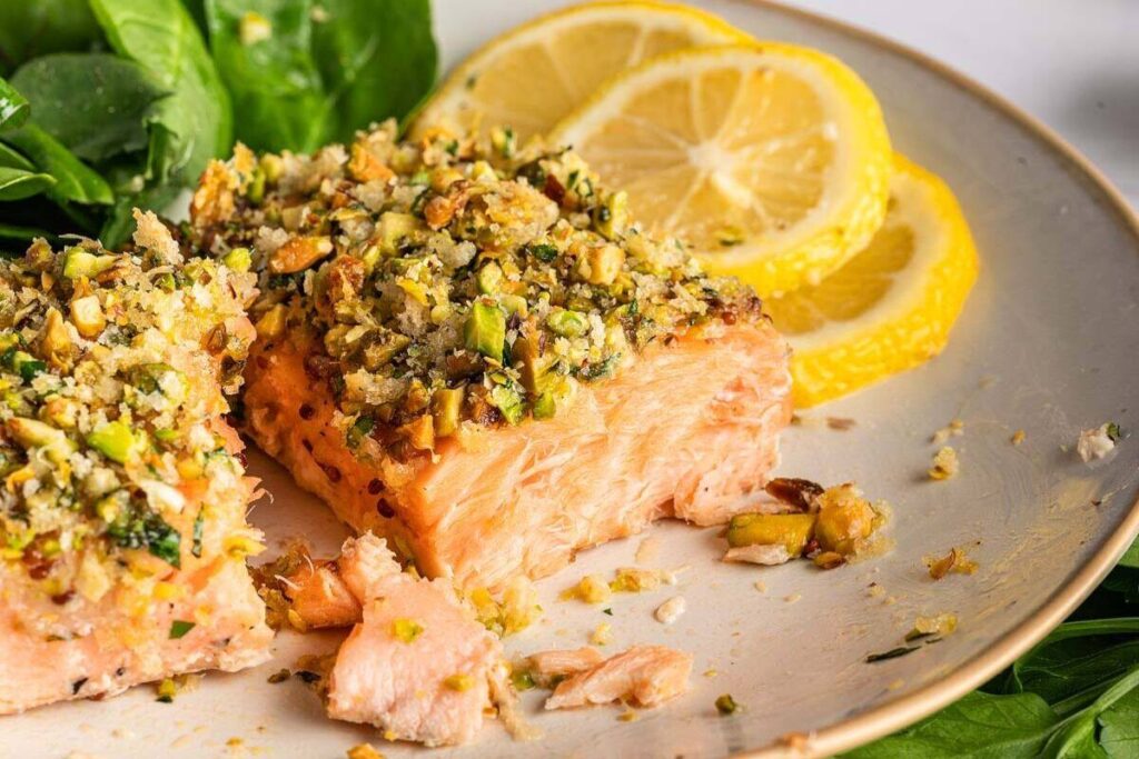 A plate of pistachio-crusted salmon graced with fresh lemon slices and a side of vibrant greens.