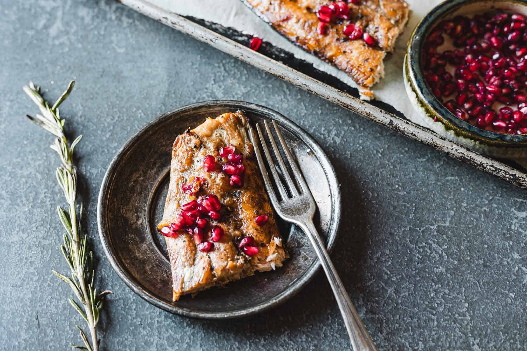 A plate with a piece of pomegranate glazed salmon garnished with pomegranate seeds and a fork.