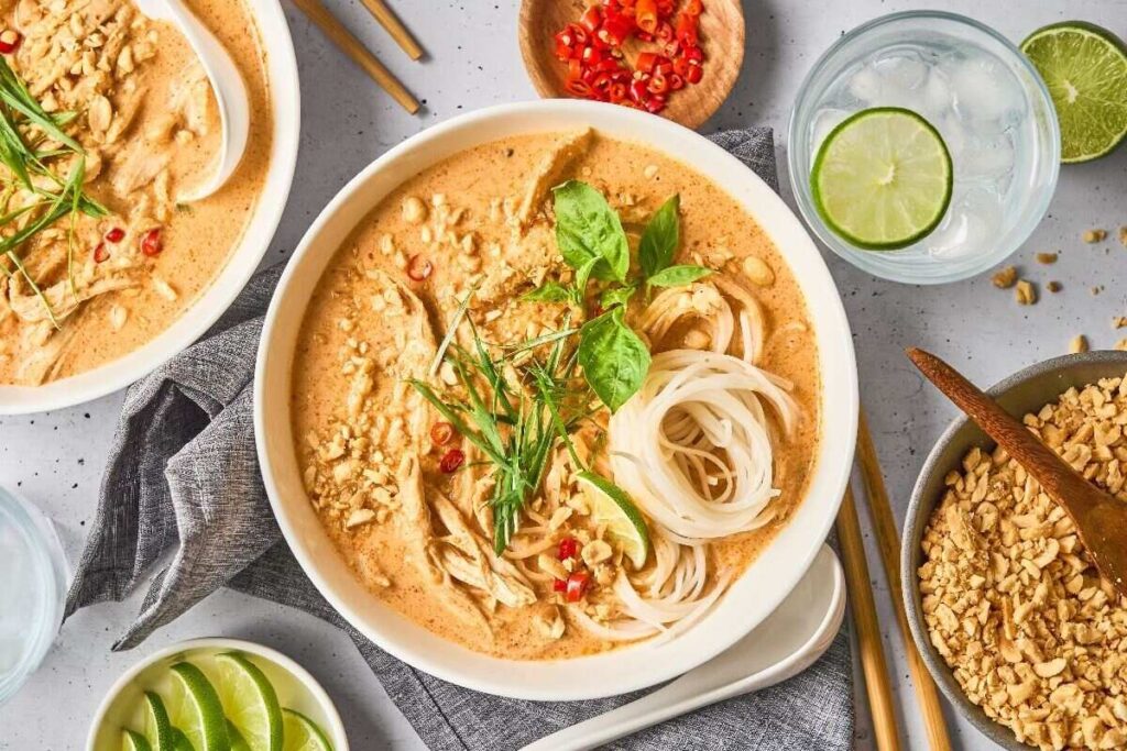 A bowl of noodle soup with herbs, peanuts, lime, and chili.