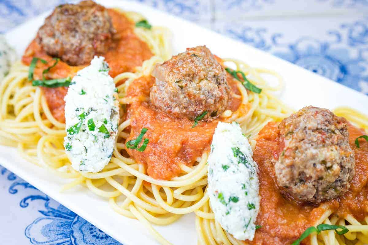 A white plate featuring spaghetti topped with ricotta meatballs and rich tomato sauce.