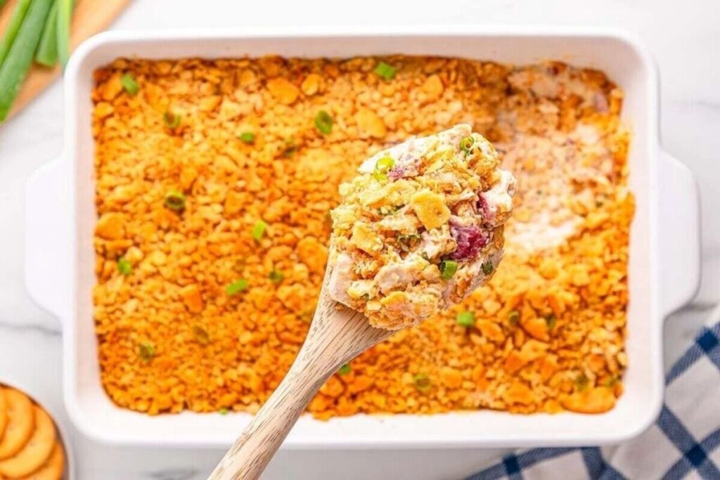 A wooden spoon lifts a cheesy, golden Ritz Cracker Chicken Casserole with a crunchy topping.