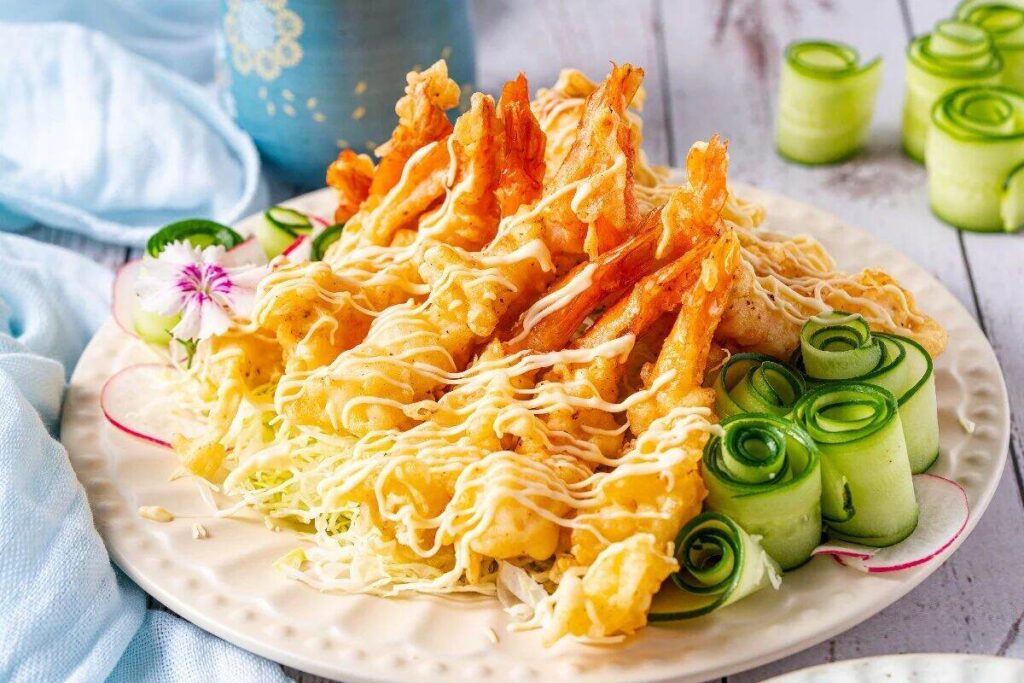 Crispy shrimp tempura with sauce, served alongside cucumber rolls and a flower garnish.