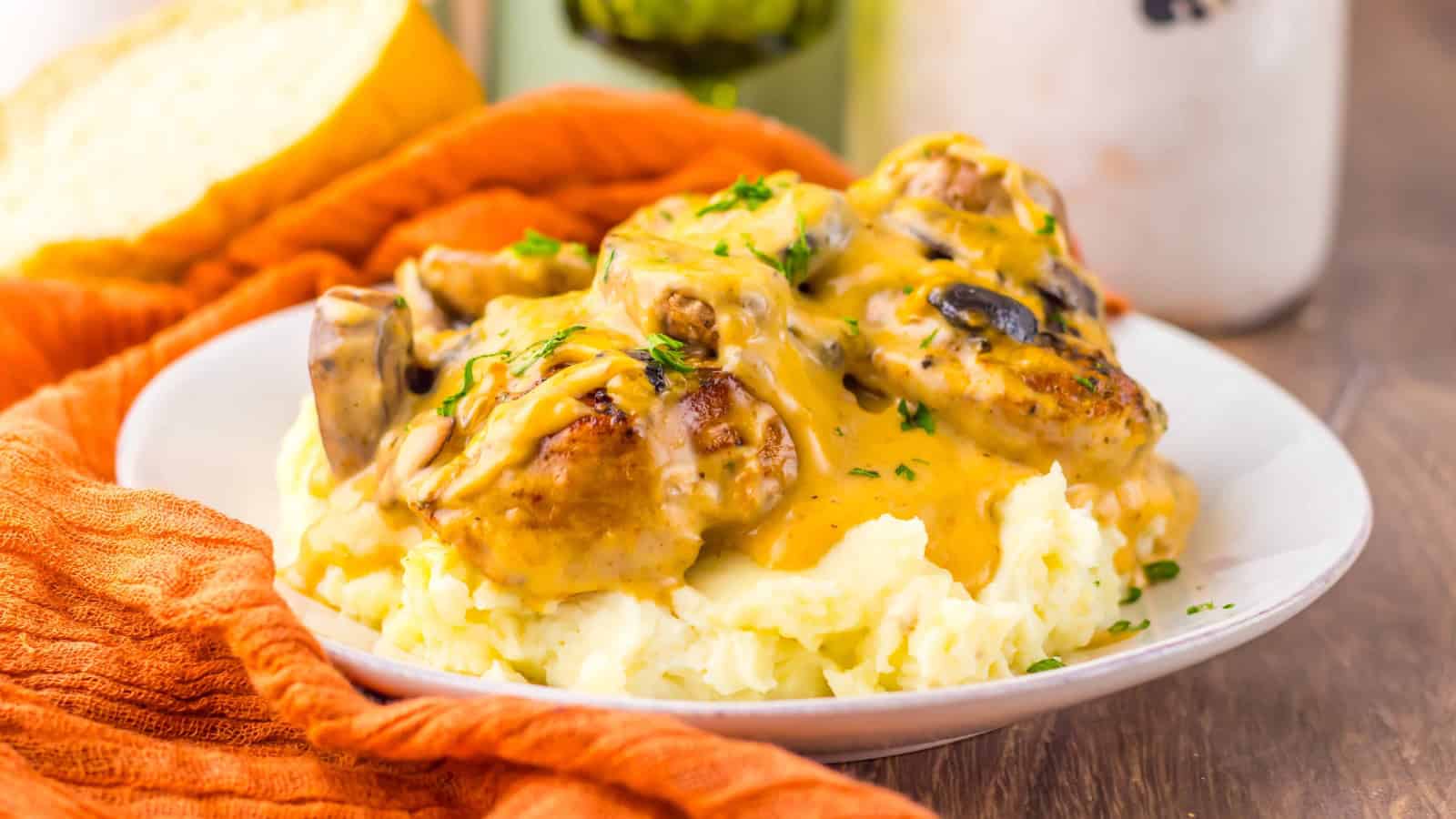 Plate of mashed potatoes topped with chicken, mushrooms, and creamy gravy, garnished with chopped herbs.
