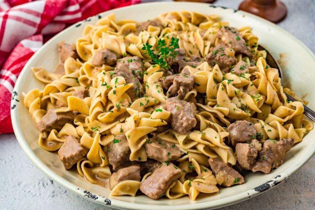 A plate of slow cooker beef stroganoff with egg noodles, garnished with chopped parsley.