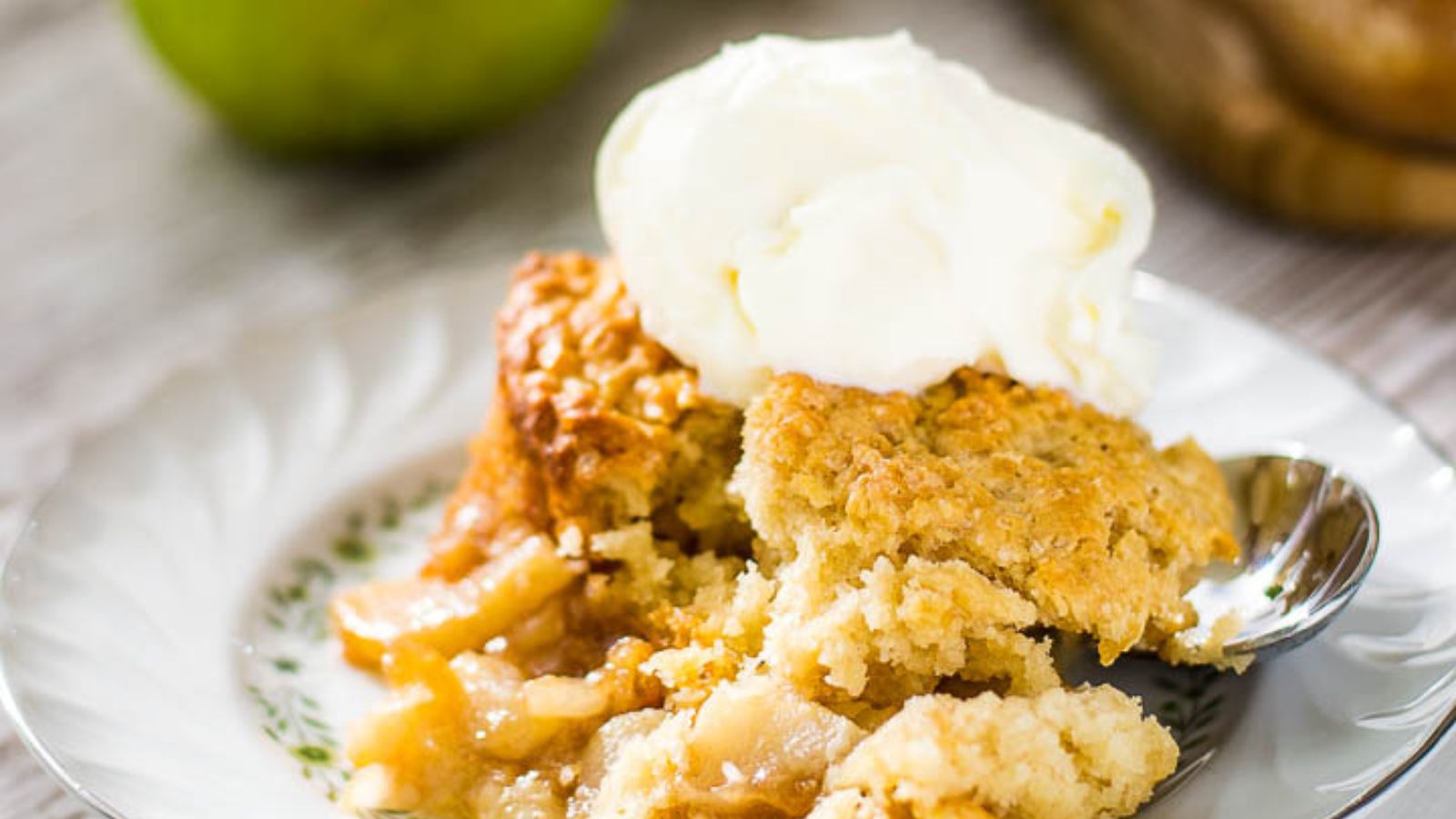 A spoonful of oatmeal with diced apples hovers above a white bowl filled with creamy oatmeal.