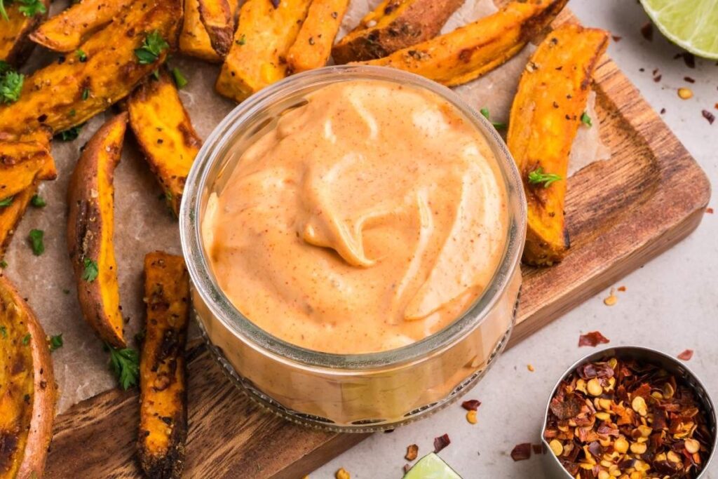 A bowl of creamy, spicy mayo dip on a wooden board.