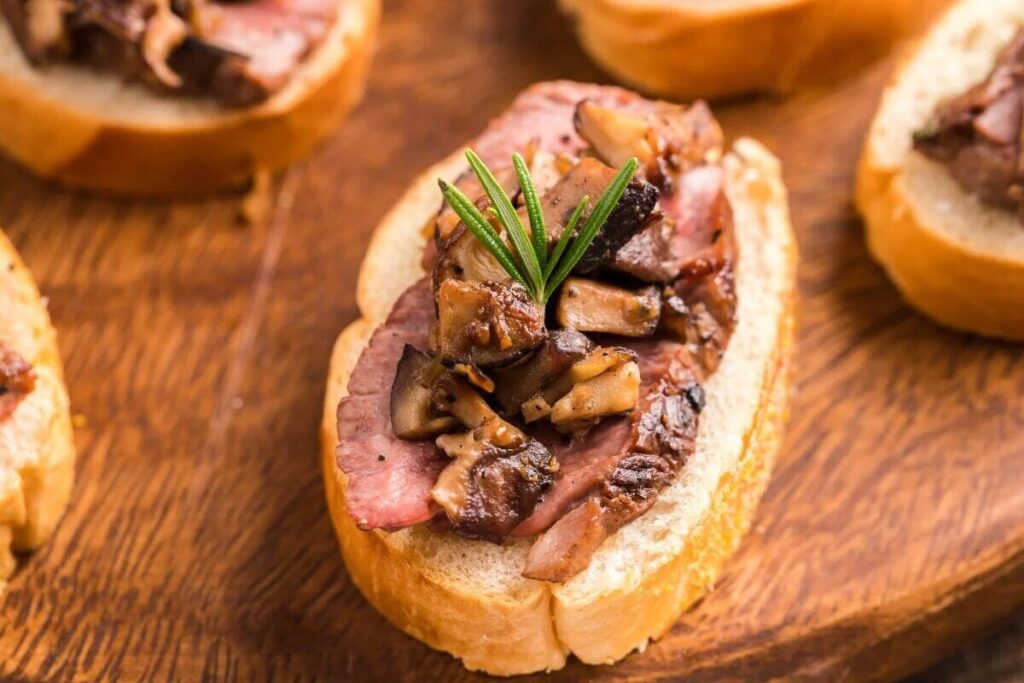 Beef and mushroom crostini topped with rosemary on a wooden board