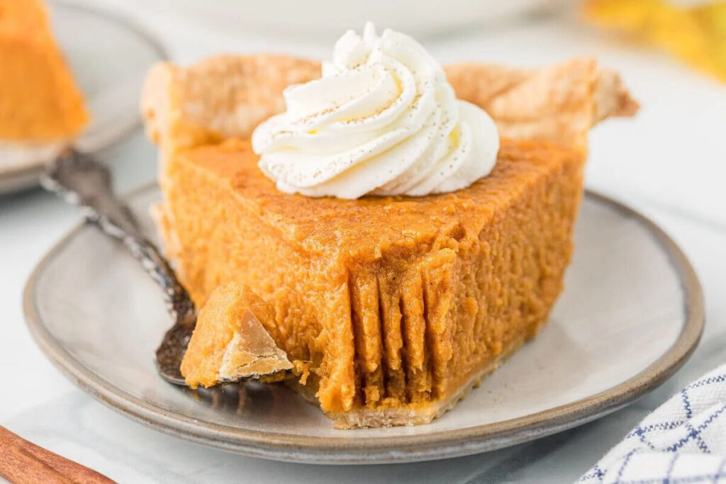 A slice of sweet potato pie with a dollop of whipped cream on top.