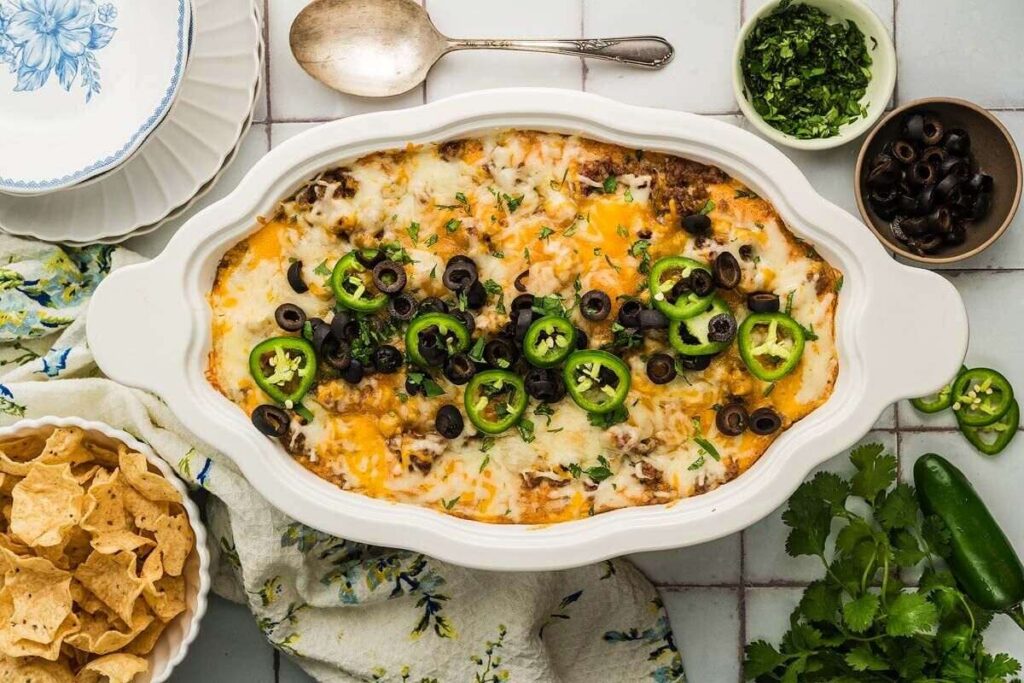 Texas Trash Dip casserole with melted cheese, black olives, jalapeños, and chips on the side.